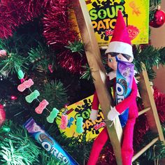 the elf is hanging on the ladder next to the christmas tree with candy bars and candies