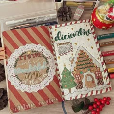 an open notebook with christmas cards and other items on the table next to some pine cones