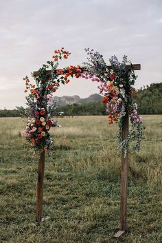 two wooden poles with flowers and greenery on them in an open grassy field,