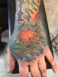 a person's hand with a tattoo on it and an image of a volcano in the sky