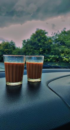 two shot glasses sitting on the dashboard of a car, with trees in the background