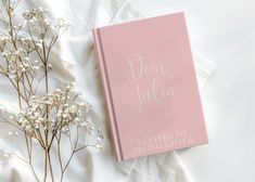 a pink book that says dear julia letters to my daughter on it next to some baby's breath flowers