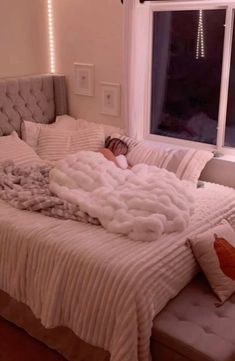 a person is sleeping on a bed with white sheets and pillows in front of a window