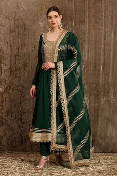 Emerald green anarkali with gota, dabka, dori, badla embroidered chevron motifs. Paired with churidar pant, dupatta and embroidered belt. 
Component: 4
Pattern: Embroidery
Type Of Work: Gota, dabka, dori, badla, chevron
Neckline: Round
Sleeve Type: Full sleeves
Fabric: Georgette, raw silk, silk chanderi, silk organza, shantoon, taffeta
Color: Green
Other Details: 
Tassel bordered sheer dupatta
Embroidered belt
Cutwork border
Occasion: Bride - Aza Fashions Angrakha Anarkali, Suits For Women Indian, Green Anarkali, Embroidered Anarkali, Embroidered Belt, Green Suit, Green Hand, Indian Fashion Designers, Silk Organza