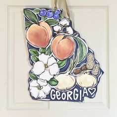 a state shaped ornament hanging on a door with flowers and fruit painted on it