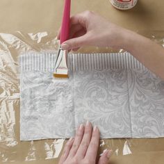 someone is using a pink brush to paint the paper on top of a piece of cardboard