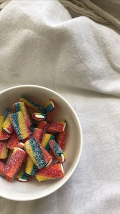 a white bowl filled with colorful candy on top of a table next to a towel