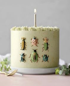 a cake decorated with bugs and candles on a table next to greenery or flowers