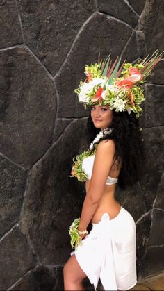 a woman wearing a hula skirt and flower headdress standing in front of a stone wall