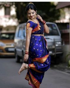 a woman in a blue and gold sari walking down the street with her hand on her hip