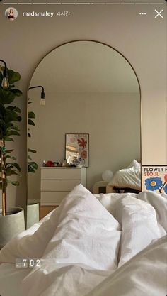 a bed with white sheets and pillows in a bedroom next to a large arched mirror