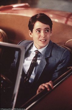 a young man in a suit and tie sitting in a car with his hand on the door handle