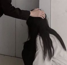 a woman with long black hair standing next to a white wall