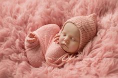 a newborn baby is sleeping on a pink fluffy blanket wearing a knitted hat and sweater