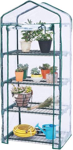 a green house filled with plants on top of a white wall and two yellow hoses next to it