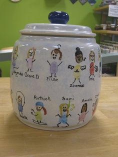 a ceramic jar with pictures on it sitting on top of a wooden table in front of a green wall