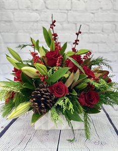 a white vase filled with red flowers and greenery on top of a wooden table