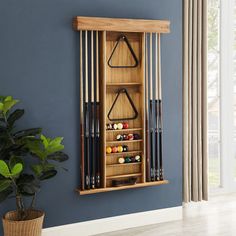 a wooden rack with pool balls and cues in it next to a potted plant