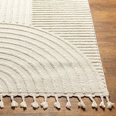 a white rug with tassels on top of a wooden floor in a room