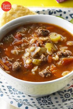 a white bowl filled with soup next to a piece of bread on top of a blue and white plate