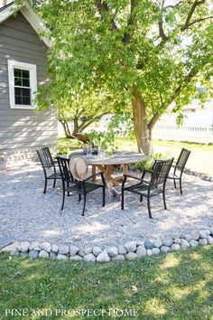 a table and chairs sitting on gravel in front of a tree