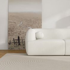 a white couch sitting on top of a wooden floor next to a wall with a painting