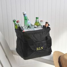 a black cooler bag filled with bottles on top of a white bench next to a straw hat