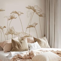 a bed with lots of pillows on top of it next to a wall with flowers painted on it