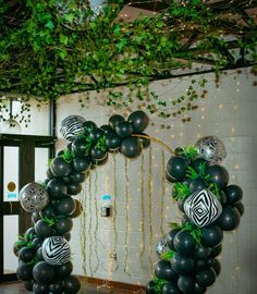 black and white balloons are arranged in the shape of an arch with greenery on it