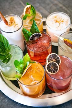 several different types of cocktails on a plate with garnishes and leaves