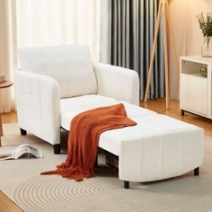 a living room with a white couch and ottoman on the floor in front of a curtained window