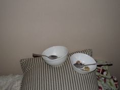 two bowls with spoons are sitting on a striped pillow