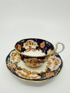 an antique tea cup and saucer with floral designs on the rim, set against a white background