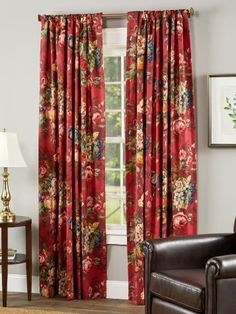 a living room filled with furniture and a window covered in red floral drapes next to a brown chair