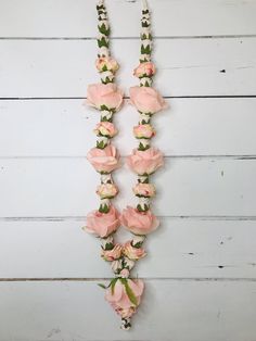 a necklace with pink flowers hanging from it's sides on a white wooden wall