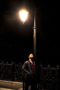 a man standing under a street light at night with his head up in the air