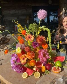 a woman standing next to a table filled with fruit and flowers