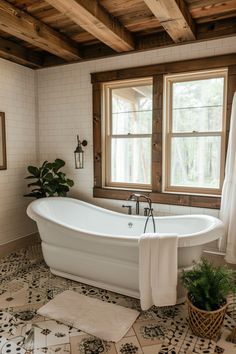 a white bath tub sitting in a bathroom next to two windows and a potted plant