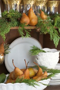 a white bowl filled with pears on top of a wooden table next to plates and silverware