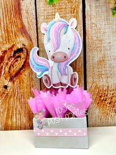 a card with a unicorn on it sitting in a box next to some pink flowers