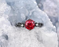 a ring with a red stone surrounded by white diamonds on top of some ice crystals