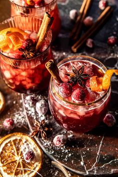 two glasses filled with cranberry punch on top of a table next to sliced oranges and cinnamon sticks