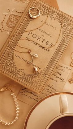 an old book with some gold jewelry on it next to a cup and saucer