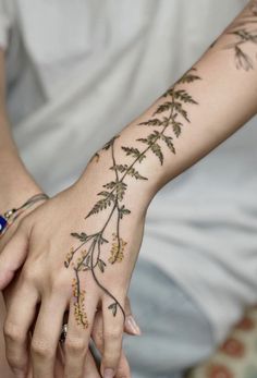 a woman's hand with tattoos on it and flowers on the wrist, holding onto her arm