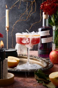 an apple cider cocktail on a tray next to candles and other fruit, with a bottle of booze in the background