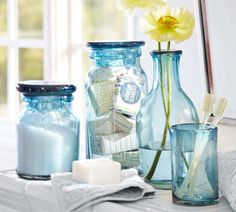 three vases with flowers in them sitting on a window sill next to soap and toothbrushes