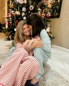 two women hugging each other in front of a christmas tree