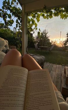 a person laying in a hammock reading a book with the sun setting behind them