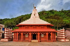 a red and white temple in front of a green hill with trees on the side