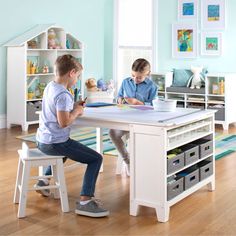 two children sitting at a table playing with toys in a room filled with blue walls